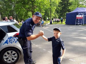 Chłopiec przebrany za policjanta wita się z policjantem na tle radiowozu.