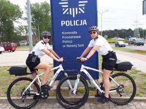 Dwie policjantki na rowerach na tle banera z napisem Policja; Komenda Powiatowa Policji w Nowej Soli.