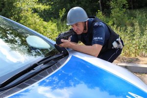 Policjant oparty o maskę radiowozu trzyma w ręku broń