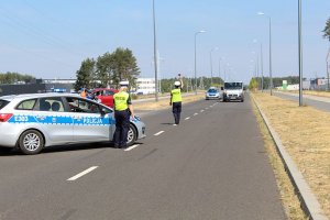 Radiowóz w oddali obok stoi dwóch policjantów