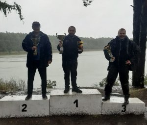 Zwycięzcy zawodów wędkarskich na podium z pucharami.