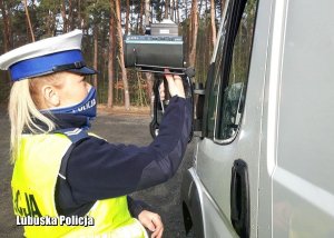 Na zdjęciu policjantka pokazuje zatrzymanemu do kontroli drogowej ręczny miernik prędkości, na którym widnieje przekroczona dopuszczalna prędkość.
