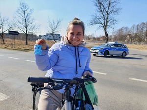 Na zdjęciu kierująca rowerem trzyma w ręku odblaskowego misia, w tle radiowóz policyjny.