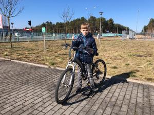 Na zdjęciu chłopiec na rowerze trzyma w ręku odblaskowego misia.