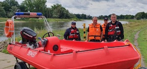 Policjant wraz ze strażakami na tle motorówki.