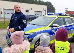 Dzieci z policjantem na tle radiowozu.