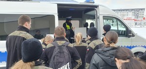 Policjantka wydziału ruchu drogowego prowadzi zajęcia zachęcające do wstąpienia do Policji dla klasy mundurowej i prezentuje im radiowóz.