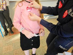 Policjantki przy stoisku promującym służbę w Policji przykleja dziewczynce serduszko Wielkiej Orkiestry Świątecznej Pomocy.