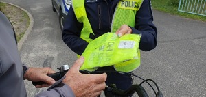 Policjantka wręcza niechronionemu na rowerze kamizelkę odblaskową.