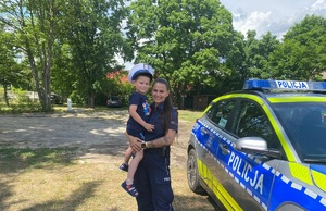 Policjantka z chłopcem na tle radiowozu.