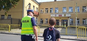 Policjant wydziału ruchu drogowego przeprowadza dzieci przez ulicę.