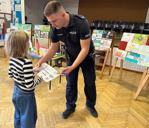 Dzielnicowy wręcza dziecku prezent za konkurs o bezpieczeństwie.