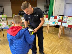 Dzielnicowy wręcza dziecku prezent za konkurs o bezpieczeństwie.