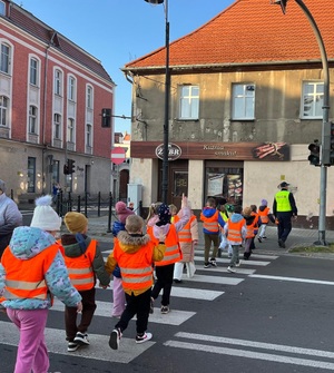 Policjanci z dziećmi przechodzą przez przejście dla pieszych.