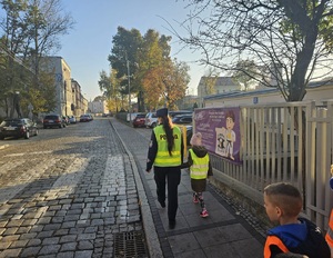 Policjanci z dziećmi przechodzą przez przejście dla pieszych.