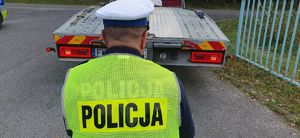 Policjant Wydziału Ruchu Drogowego sprawdza oświetlenie pojazdu zatrzymanego do kontroli drogowej.