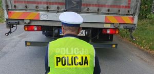 Policjant Wydziału Ruchu Drogowego sprawdza oświetlenie pojazdu zatrzymanego do kontroli drogowej.