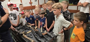 Dzieci słuchają jak instruktor strzelania opowiada o swojej profesji.