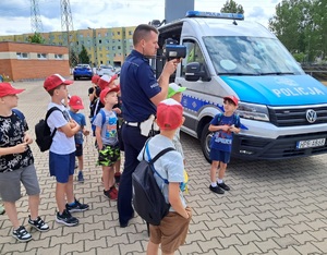 Policjant wydziału ruchu drogowego pokazuje dzieciom busa policyjnego.
