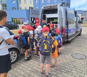 Policjant ruchu drogowego pokazuje dzieciom busa policyjnego.