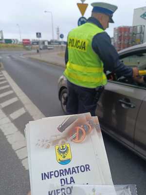 Ulotki informacyjne na tle policjanta sprawdzającego trzeźwość kierowców.