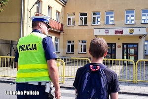 Policjant przeprowadza dziecko przez przejście dla pieszych.