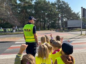 Policjant uczy dzieci prawidłowo przechodzić przez przejście dla pieszych.